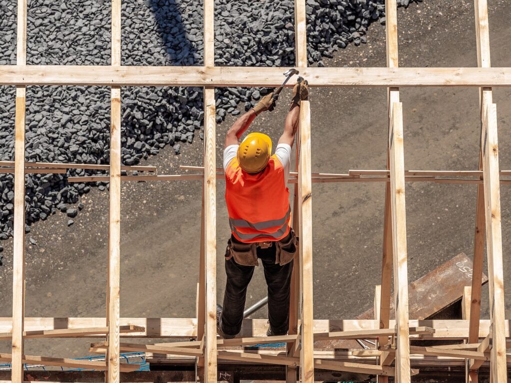 Zimmermann mit Helm und Warnweste befestigt Holzlatten auf einer Baustelle
