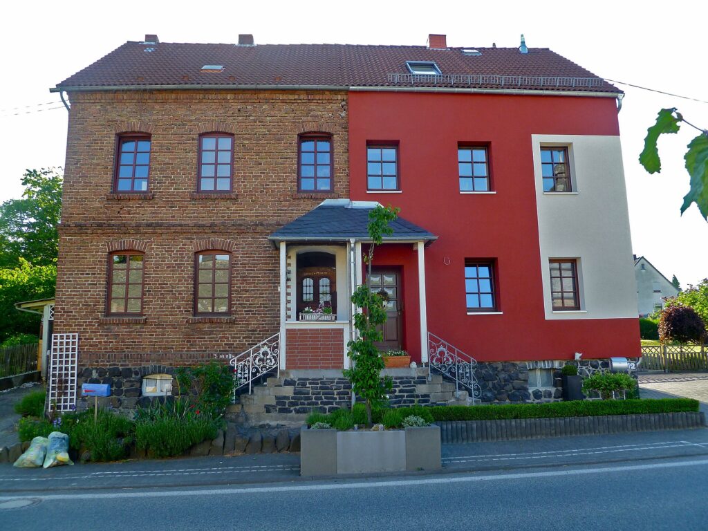 Älteres Backsteinhaus, dessen eine Haushälfte mit Dämmung und rotem Verputz erneuert wurde