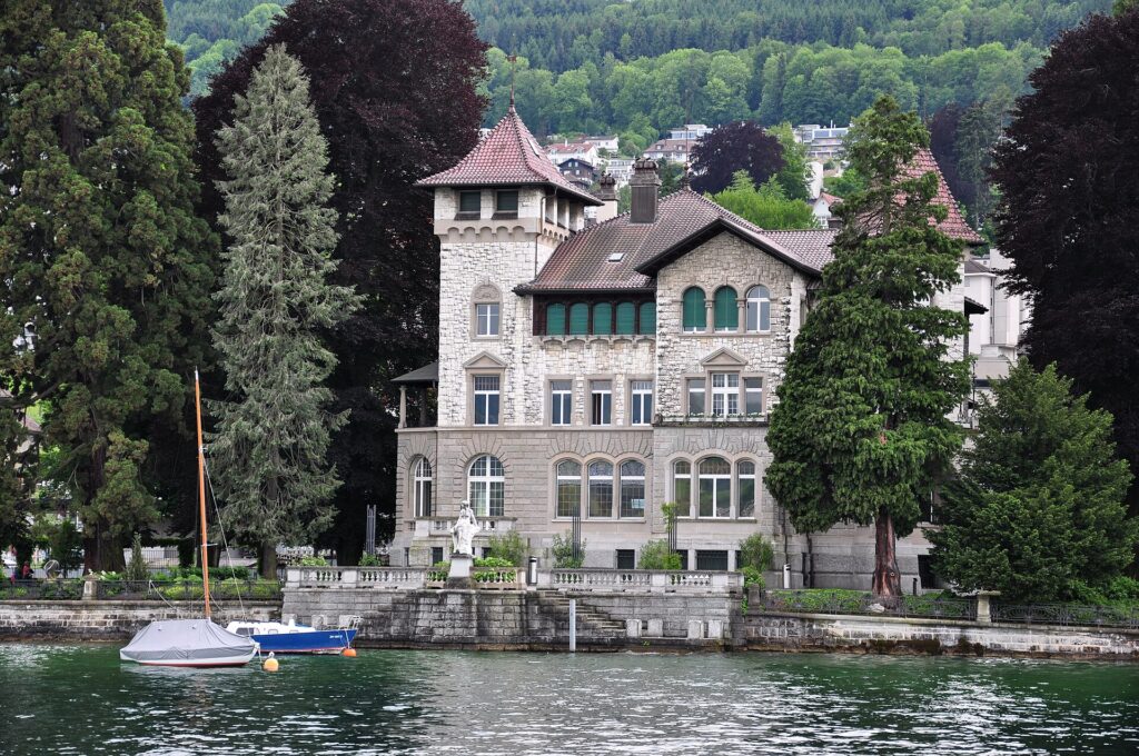 Traditionelle Villa mit Natursteinfassade und Turm direkt am Zürichsee, davor eine Ufermauer mit Treppe